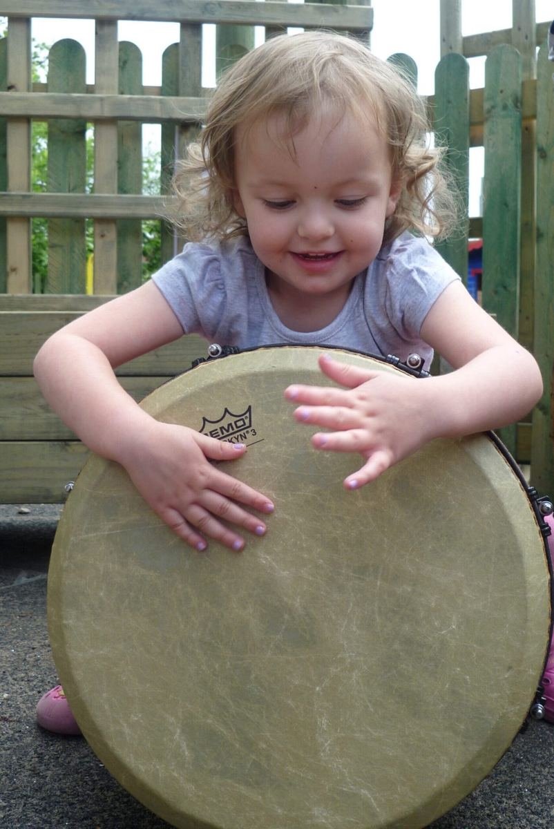 A smiling toddler playing a large djembe drum